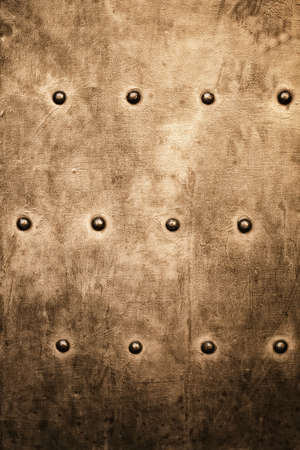 Closeup of grunge gold brown metal plate with rivets and screws as background or textureの写真素材