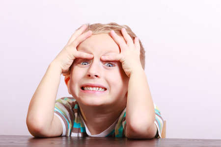 Portrait of surprised angry emotional blond boy. Child kid making silly funny face at the table interior. Emotions.の写真素材