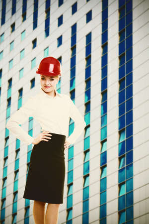 Attractive female engineer and modern futuristic glass building  Woman architect in red safety helmet  Construction site の写真素材