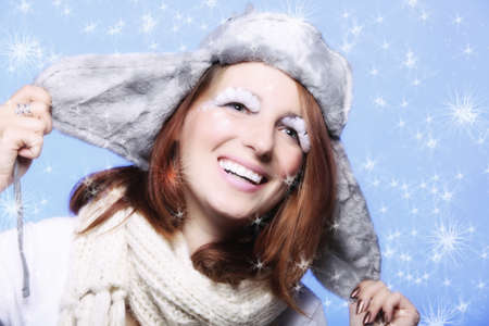 Fashion woman red haired girl in warm clothing fur hat stylish creative make up false long white eye lashes on blue winter snow flakes の写真素材