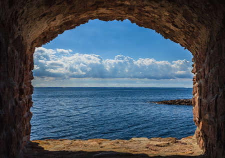 View of blue sea and sky from hole in old stonewall wall  Seascape in stone window casing frame  Travel tourism の写真素材