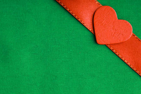 Valentine's day. Red wooden decorative heart love symbol on green cloth textile background with ribbon. Blank copy spaceの写真素材