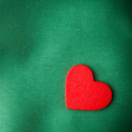 Valentine's day. Red wooden decorative heart love symbol on green cloth textile background with blank copy spaceの写真素材