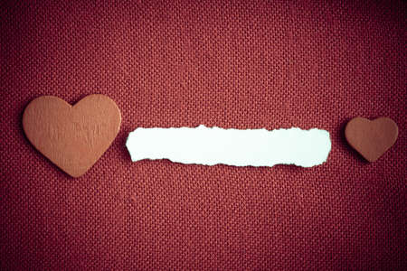 Piece scrap of white paper blank copy space and hearts symbols of love on red fabric textile...