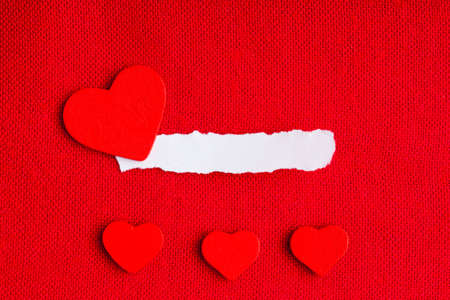 Piece scrap of white paper blank copy space and hearts symbols of love on red fabric textile material background. Valentines day.の写真素材