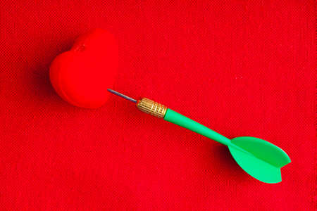 Blank copy space and hearts symbols of love with green dart on red fabric textile material background. Valentines day.の写真素材