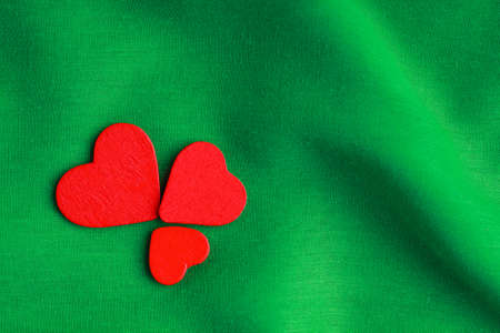 Red wooden decorative hearts on abstract green wavy folds cloth or textile elegant materialの写真素材