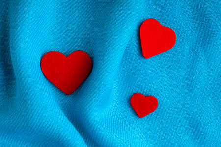 Red wooden decorative hearts on abstract blue wavy folds cloth or textile elegant materialの写真素材