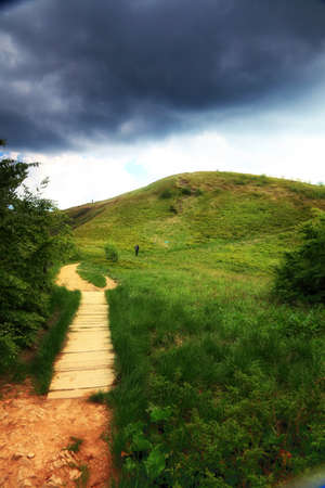 Beautiful summer landscape in the mountains. Pathway through the grassy hills, dark sky with clouds...