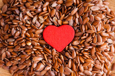 diet healthcare concept. Brown raw flax seeds linseed as natural background and red heart symbol. Healthy food  for preventing heart diseases. Flaxseeds are full of omega-3 fatty acids.の写真素材