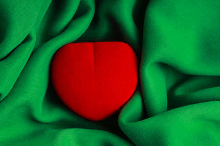 Red jewel box heart shaped gift present on green fabric abstract cloth wavy folds of textileの写真素材