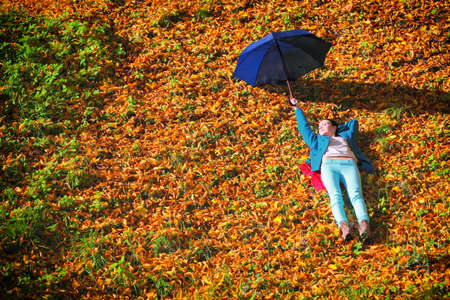fall lifestyle concept  casual young woman girl relaxing with blue umbrella in autumnal park  golden colorful leavesの写真素材