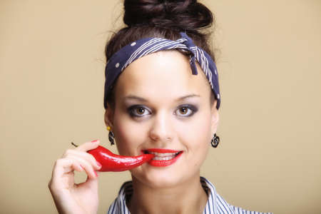 Beautiful seductive woman with red lips holding chilli pepper studio shot brown backgroundの写真素材