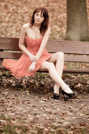 Full length fashionable young woman in red dress outdoor relaxing in park sitting on bench vintage photo sepia toneの写真素材