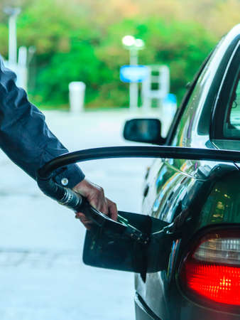 Male hand refilling the car with gas or petrol on filling station, holding a fuel pump outdoorの写真素材