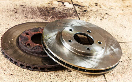 Auto in service. New and old front brake disks for modern car lying on floor in mechanic garage car service.の写真素材