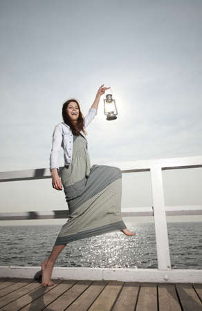 Full length young woman on pier with a oil kerosene lamp. Concept carrying light, daylightの写真素材