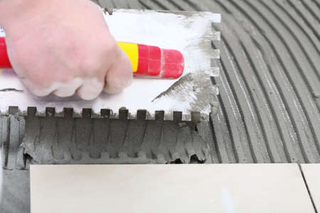 Home improvement, renovation - construction worker tiler is tiling, ceramic tile floor adhesive, ...