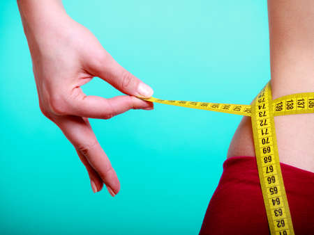 Time for diet slimming weight loss. Health care and healthy nutrition. Young fitness woman fit girl with measure tape measuring her waistline on blue greenの写真素材