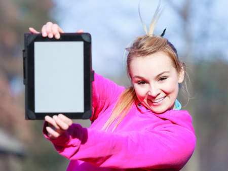 Fitness woman sport teenage girl in pink tracksuit showing blank copy space screen of tablet touchpad computer outdoor. Electronic technology.の写真素材