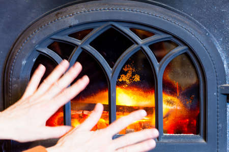 Winter at home. Woman warming her hands at fire fireplace interior. Heating.の写真素材