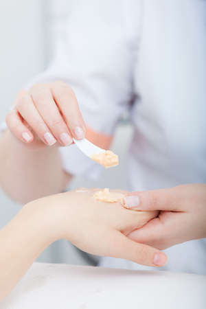Cosmetician beautician applying orange moisturizing cream balm on hands of female clientの写真素材