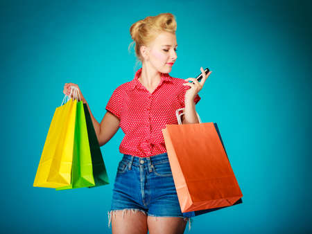 Pinup girl young woman in retro style buying clothes texting on mobile phone.