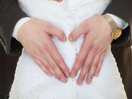 Wedding day. Closeup of male hands on back of bride in white dress. Man groom showing making heart shape love symbol. Studio shot.の写真素材