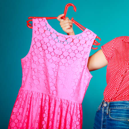 Closeup of pink dress in female hand on vibrant blue. Woman girl buying clothes. Sale and retail.の写真素材