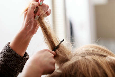 Closeup of female blond wavy hair by hairdresser  Hairstylist combing girl client  Young woman in...