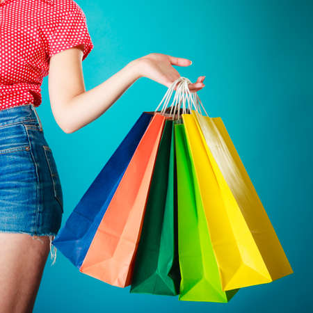 Closeup of colorful paper shopping bags in female hand on vibrant blue  Woman girl buying clothes  Sale and retail の写真素材