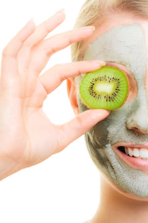 Skin care. Woman in clay mud mask on face covering eye with slice of kiwi isolated. Girl taking care of dry complexion.の写真素材