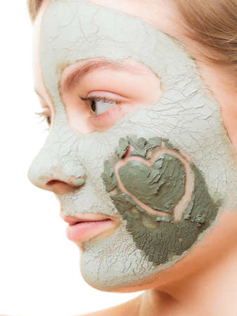 Skin care. Woman in clay mud mask with heart symbol of love on cheek isolated on white. Girl taking care of dry complexion. Beauty treatment.の写真素材