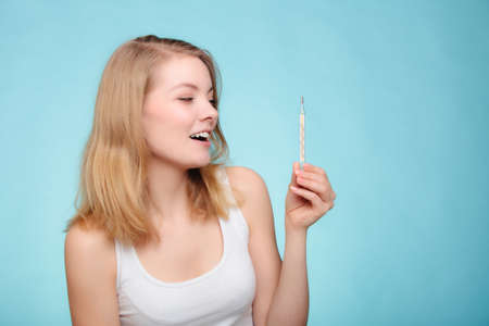 Happy woman sick girl with fever holding mercury thermometer on blue.の写真素材