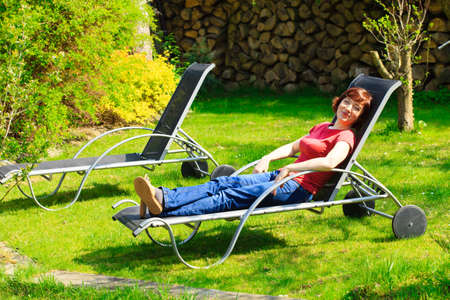 Happy mature woman relaxing resting on the black deck chair in the garden.の写真素材