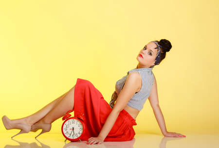 Full length of fashionable pin-up girl sexy young woman with bun and red clock on yellow  Time for...