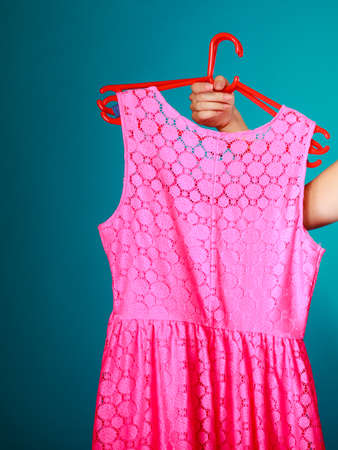 Closeup of pink dress in female hand on vibrant blue. Woman girl buying clothes. Sale and retail. Studio shot.の写真素材