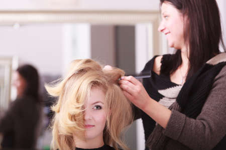 Beautiful smiling girl with blond wavy hair by hairdresser  Hairstylist with comb combing female client young woman in hairdressing beauty salon  Hairstyle の写真素材