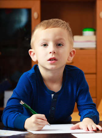 Happy childhood  Blond boy child kid with pen writing on piece of paper doing homework  At home の写真素材