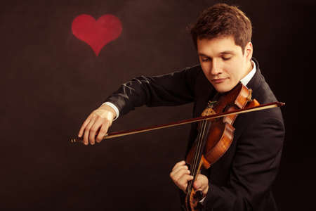 Art and artist. Young elegant in love man violinist fiddler playing violin on black background with...
