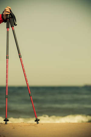 Nordic walking equipment. Closeup of red sticks on the sandy beach. Active and healthy lifestyle.の写真素材