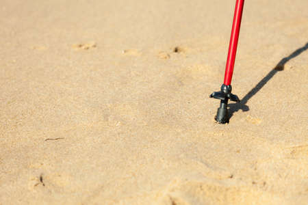 Nordic walking equipment. Closeup of red stick on the sandy beach. Active and healthy lifestyle.の写真素材