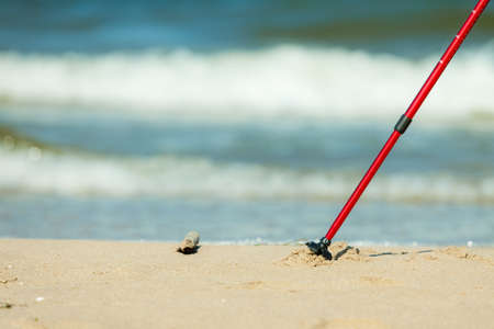 Nordic walking equipment. Closeup of red sticks on the sandy beach. Active and healthy lifestyle.