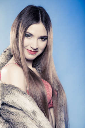 Portrait of sexy girl with long hair. Young woman in red bra underwear and fur coat on blue. Femininity. Studio shot.の写真素材