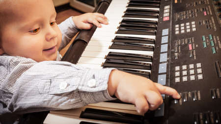 Happy childhood and music. Little boy child kid playing on the black digital midi keyboard piano synthesizer musical instrument indoor.の写真素材