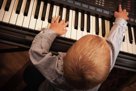 Little boy child kid playing on the black digital midi keyboard piano synthesizer musical instrument indoor.の写真素材