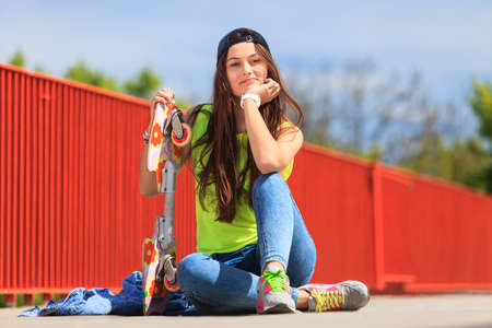 Summer sport and active lifestyle. Cool teenage girl skater sitting with skateboard on the street. Outdoor.の写真素材