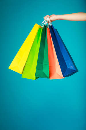 Closeup of colorful paper shopping bags in female hand on vibrant blue. Woman girl buying clothes. Sale and retail.の写真素材