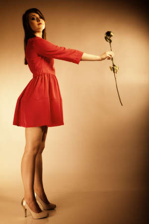 Beautiful fashion woman teen girl in red gown with dry rose. Photo in old color image style.の写真素材
