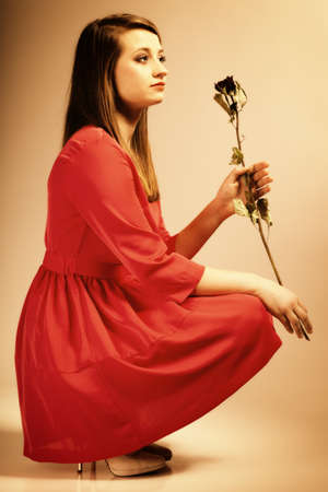 Beautiful fashion woman teen girl in red gown with dry rose. Photo in old color image style.の写真素材